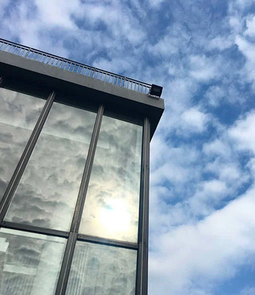 Low-angle view of a modern glass building under a bright, cloud-dappled sky.