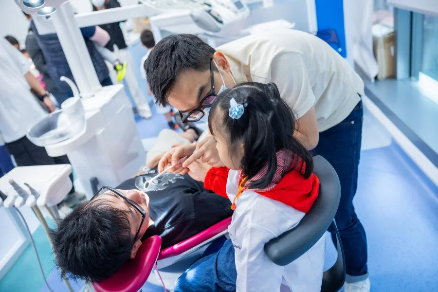 A mini-dentist conducts dental check-up on his parent under the supervision of a resident dentist.  
